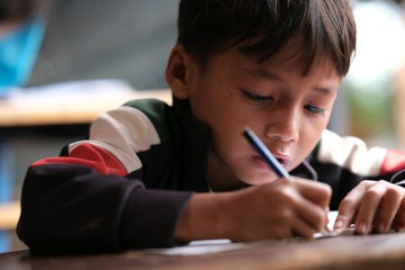 Why Wealthy Parents Are Hiring Professional Apology Writers for Their Children Child sitting at desk with pen and paper, writing
