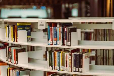 Book Banning Controversies Are Driving More Literary Sales Than Awards Ever Did Close-up view of books on library shelves with warm lighting