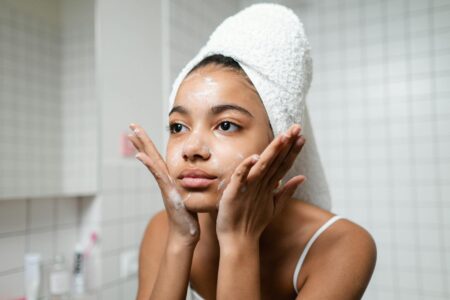 Morning Face Wash Debate Splits Skincare Community Woman washing her face with cleanser at bathroom sink
