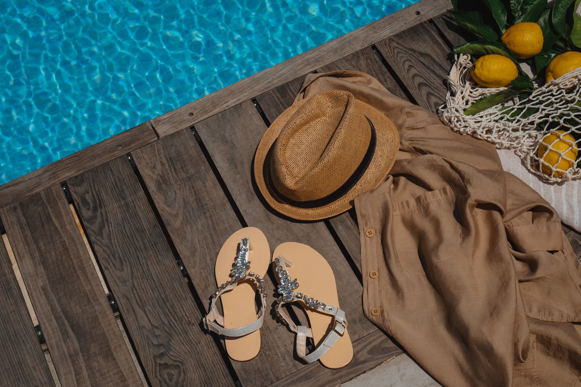 Straw bag and jelly sandals on sandy beach beside a summer dress