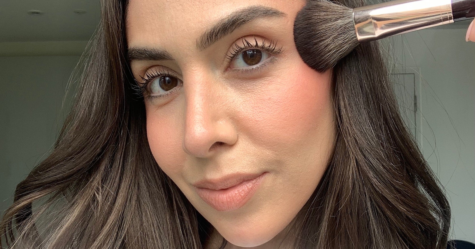 Close-up of a woman applying blush and bronzer to her cheeks with a makeup brush